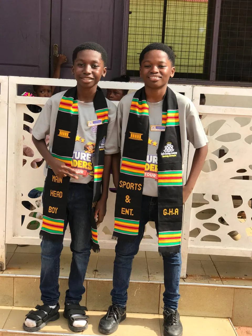 Two prefects in kente stoles standing outside the school building