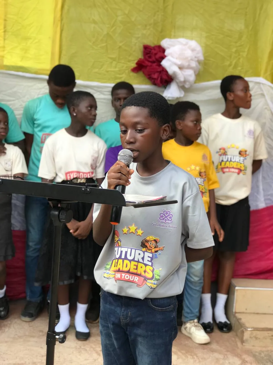 A pupil speaks at a lectern while classmates stand behind him